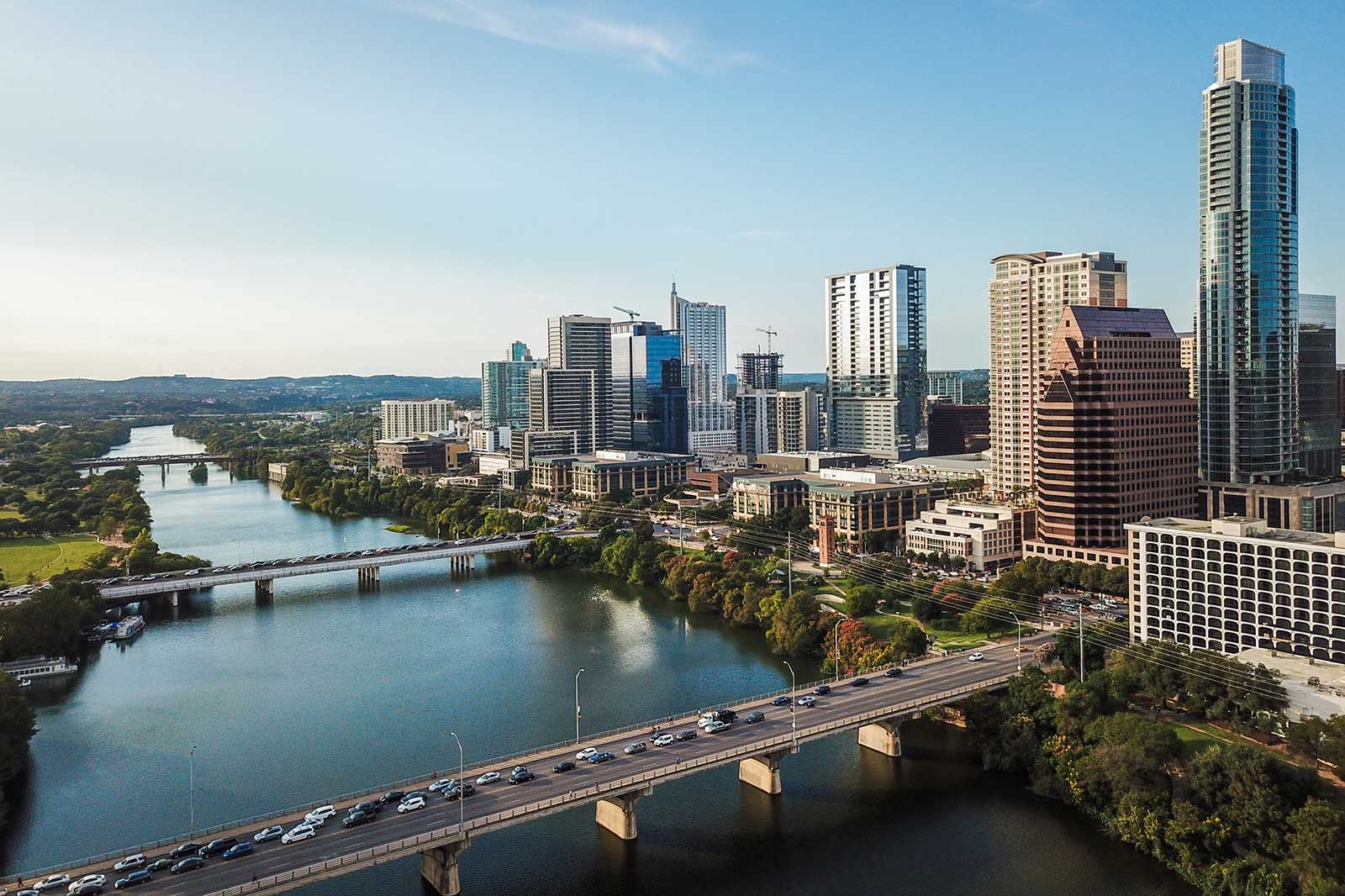 Aerial view of Austin skyline with a river and bridges amidst urban buildings and green spaces under a clear blue sky.